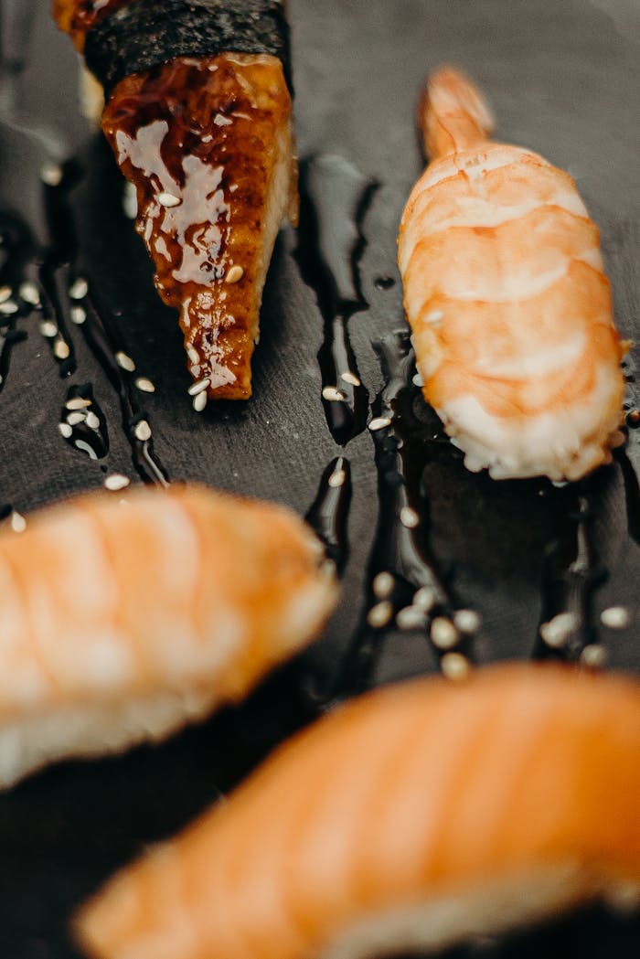 A close-up view of assorted sushi pieces on a black plate, drizzled with sauce.