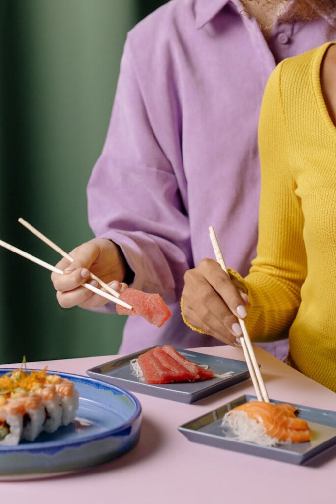 Hands enjoying fresh sushi with chopsticks at a vibrant table setting.